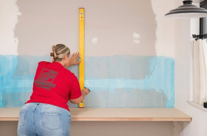 A Bunnings Team Member is using a spirit level to mark the centre line on a primed wall.