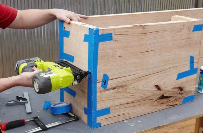 A person joining two lengths of hardwood at right angles using a nail gun