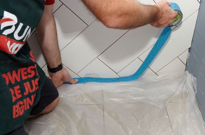 Painters tape being used to cover the floor before a wall is grouted