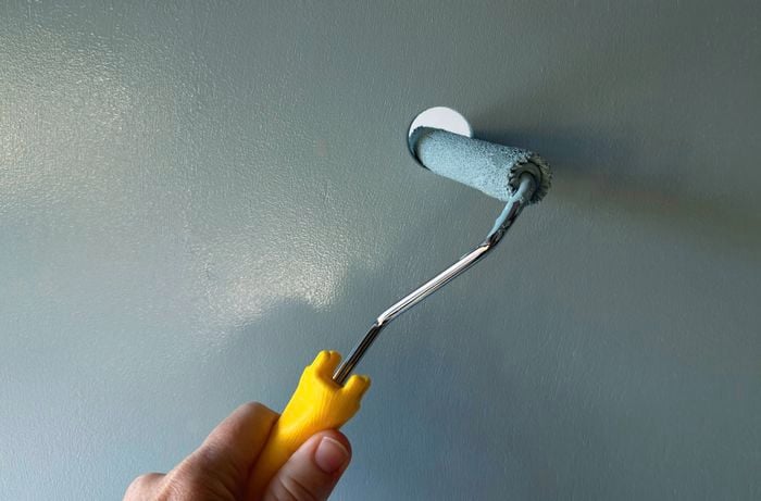 A hand using a paint roller to paint a cabinet door. 