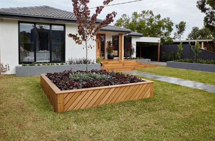 Front yard with large planter box of succulents, tiered decking steps, off white paint, and black window frames.