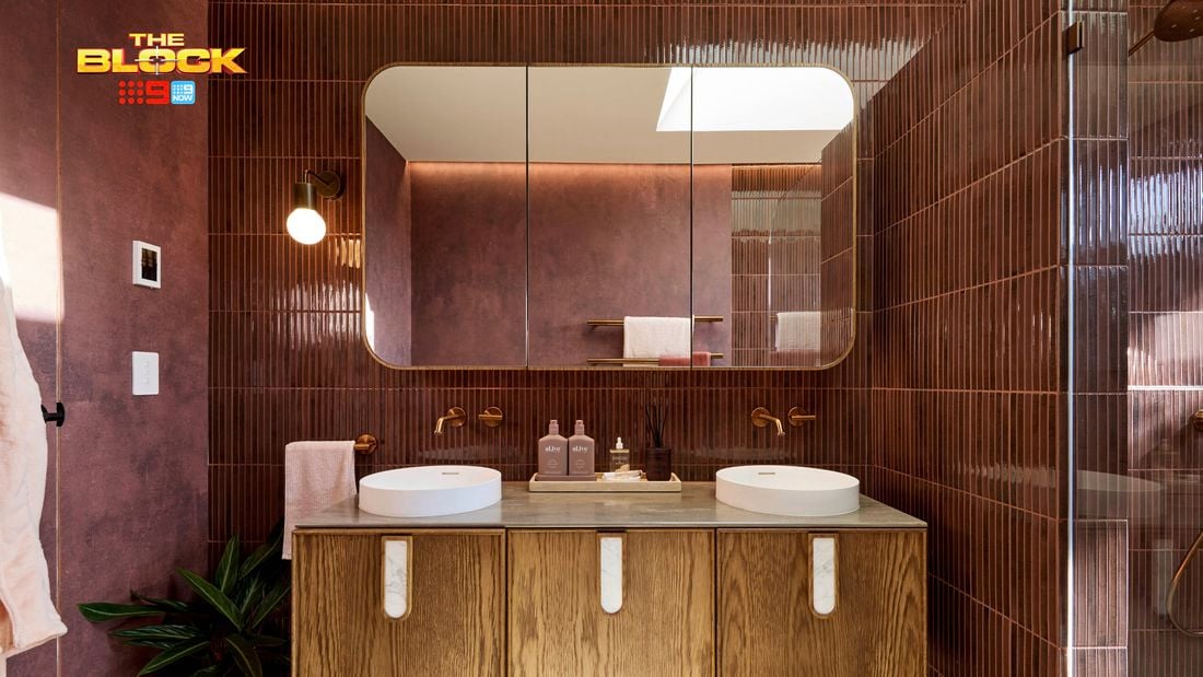 Modern bathroom with double round sinks on a wooden vanity, large mirror, maroon tiled walls, and partial view of a glass shower. 
