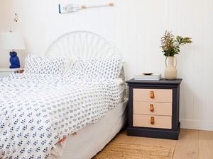 Upcycled bedside table with flower vase on top and next to a bed in the bedroom.