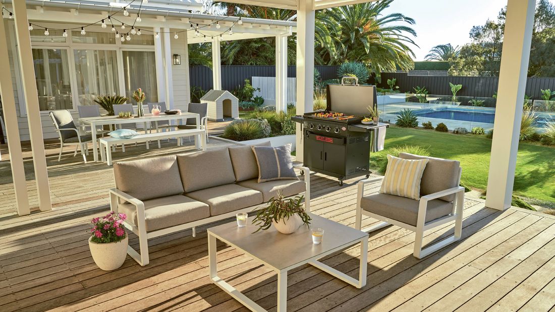 Sunny outdoor patio area with lounge, coffee table, dining set, BBQ, and dog kennel.