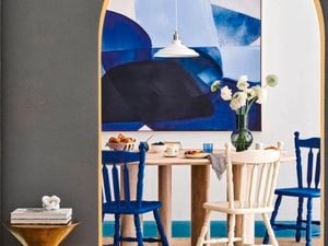 Dining room with timber round table, colourful timber chairs, flower in a vase sitting in the dining table