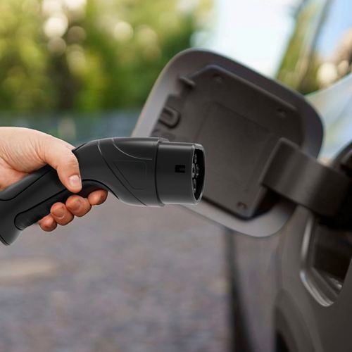 A hand holding a Arlec EV charging plug, positioned near an electric vehicle charging port.