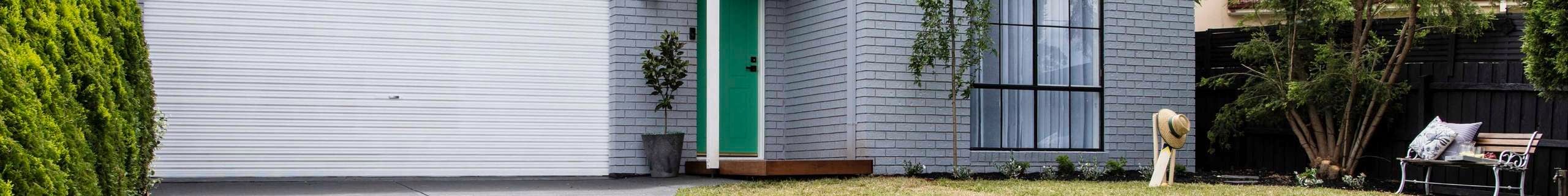 Front of brick house painted grey, with green lawn and neat garden.