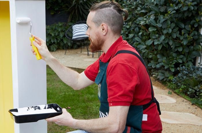 Using a roller, a man paints white onto a bookcase.