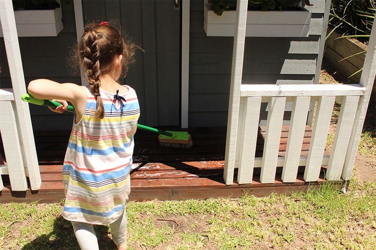 Young girl cleaning an outdoor deck with a broom