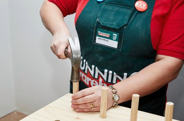 A person using a hammer to insert dowel into holes in a plywood sheet