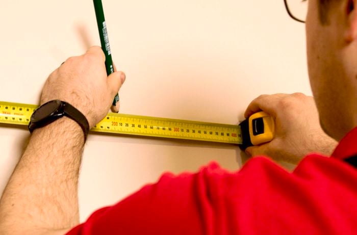 A Bunnings Team Member holding a pencil and a tape measure against a wall