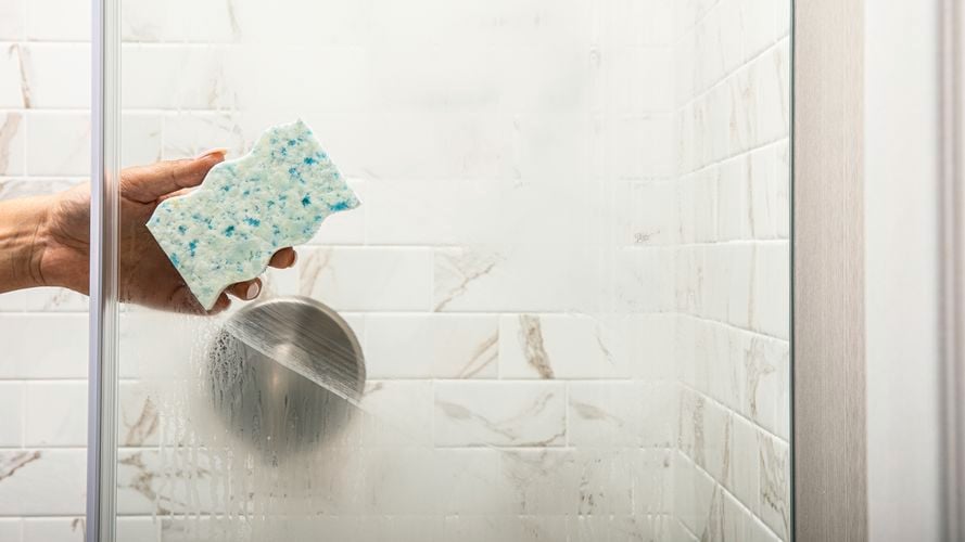A person cleaning a shower screen with the Eraser Daddy.