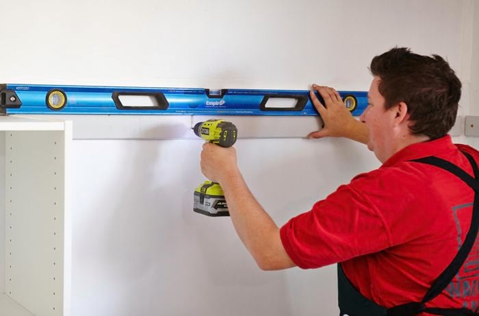 Person using spirit level to ensure cleat is drilled into wall straight.
