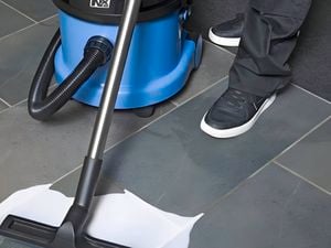 Person using a blue and black Numatic NX vacuum cleaner to clean a liquid spill on a tiled floor.