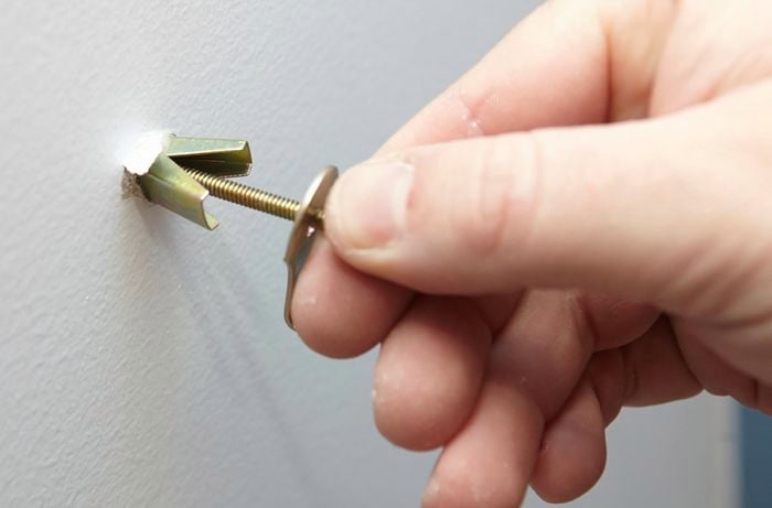 Close-up of person screwing a spring toggle into a plaster wall