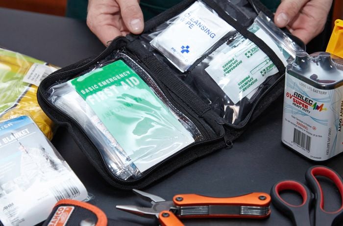 A first aid kit containing Band-Aids, cleansing wipes and other dressings, along with a battery, scissors, Swiss army tool, blanket and more