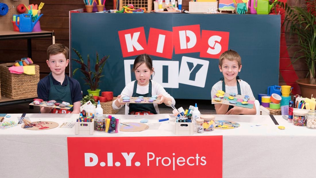 Three kids are holding their DIY tic tac toe game at the Bunnings Workshop.