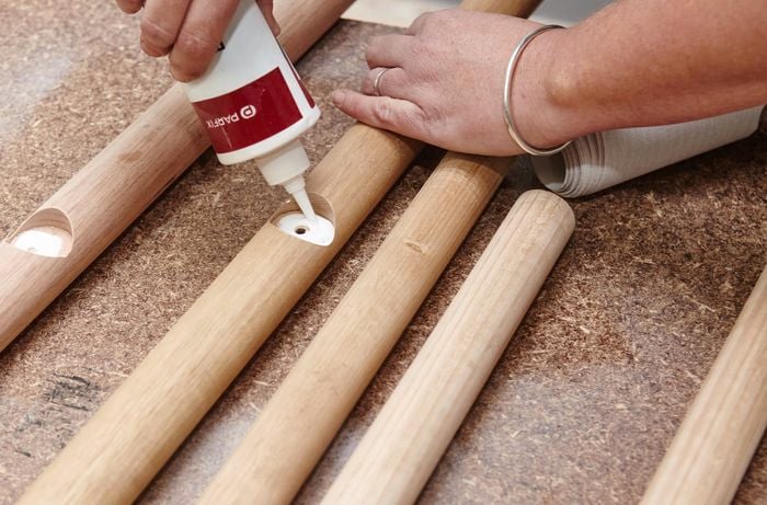 Person putting glue in hole of timber where ladder rungs will be inserted.
