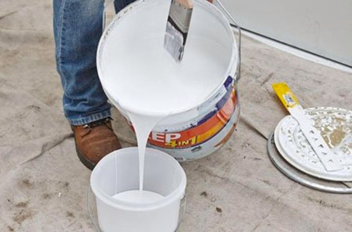 Person pouring paint into a smaller bucket.