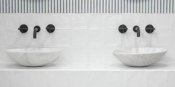 An image of a bathroom with white tiles and black tapware