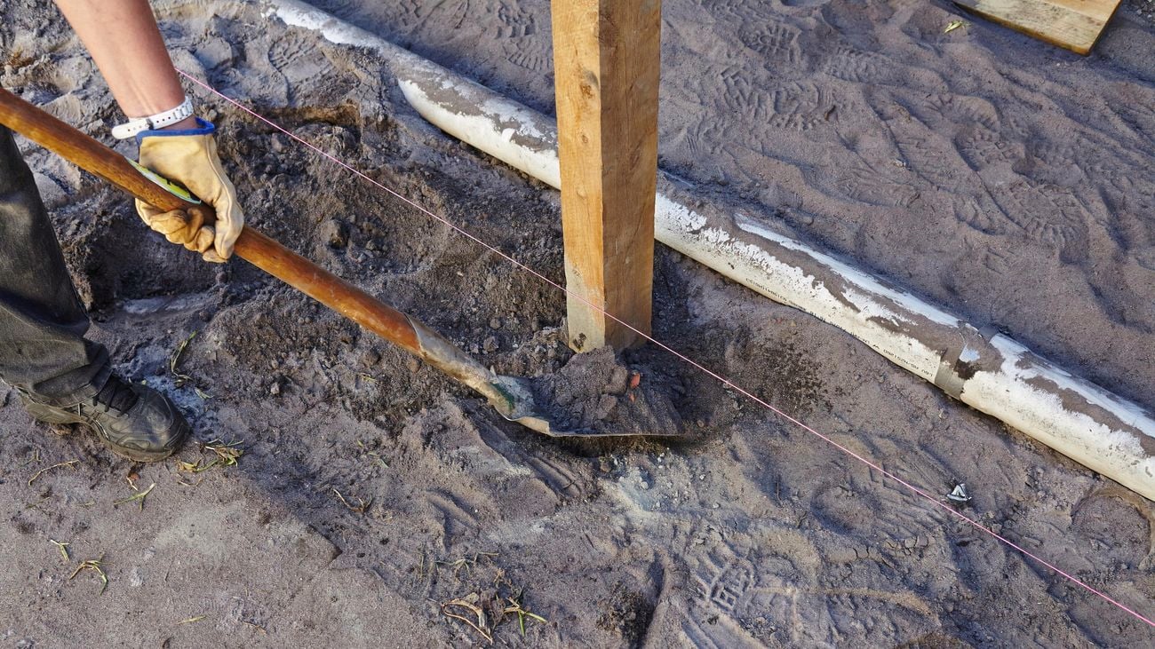 A person back-filling a post hole using a long-handled shovel