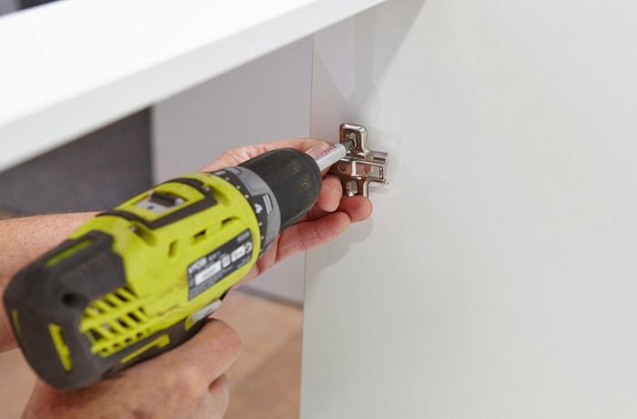 Person attaching hinges to inside of cupboard