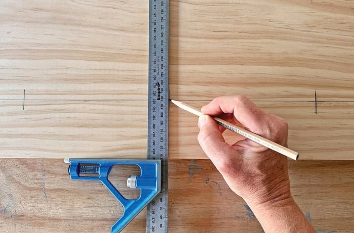 Hand holding pencil, using a ruler to markup wood.