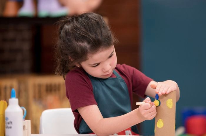 A little girl is decorating the outside of a cardboard tube.