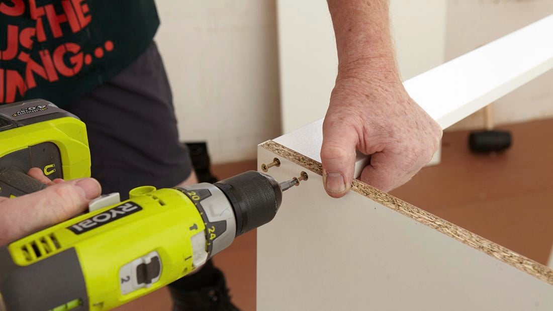 Person using a cordless driver to attach two cabinet panels
