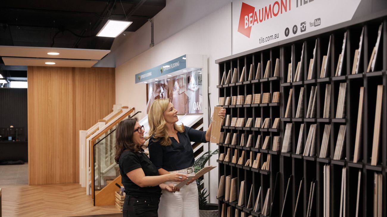 Deborah Hutton and a Bunnings Building Solutions Studio expert in a showroom with a tile sample display rack behind them.
