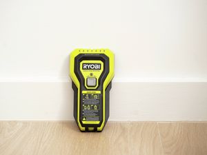 Yellow handheld stud finder standing upright against a wall.