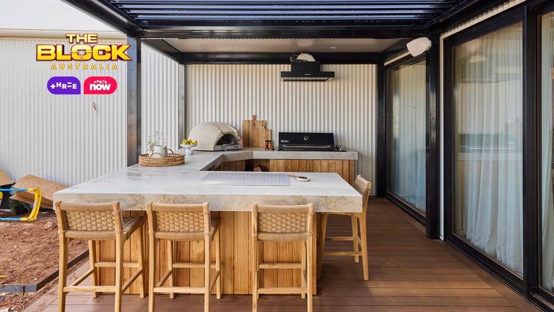 An outdoor area with a kitchen bench, with a pizza oven, barbecue on it and chairs in front of it.