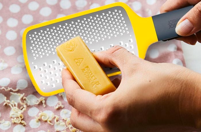 A hand grating a block of beeswax over a rectangle of patterned fabric.