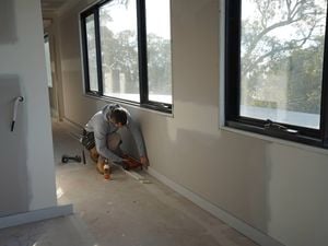 A tradesperson uses a Paslode nailer and flooring adhesive to secure floor trims in a building hallway before flooring installation.