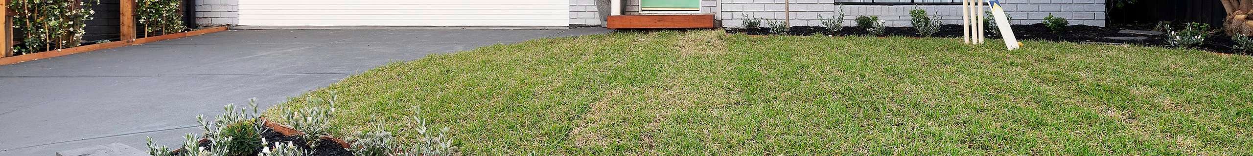 Front of brick house painted grey, with green lawn and neat garden.