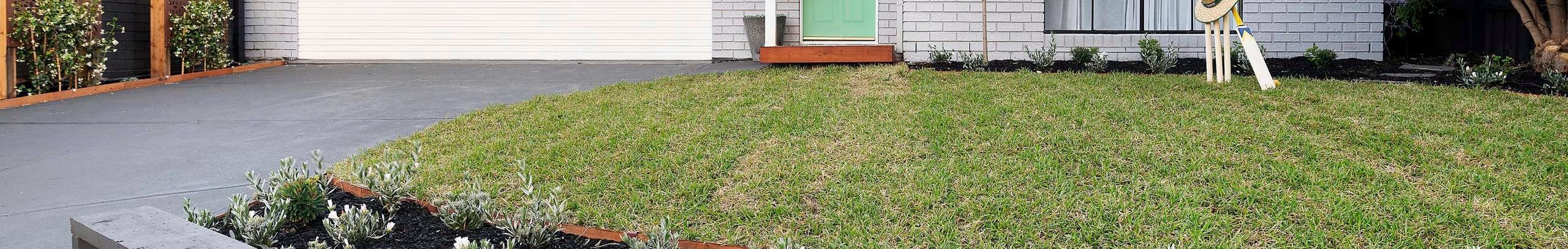Front of brick house painted grey, with green lawn, neat garden and cricket set