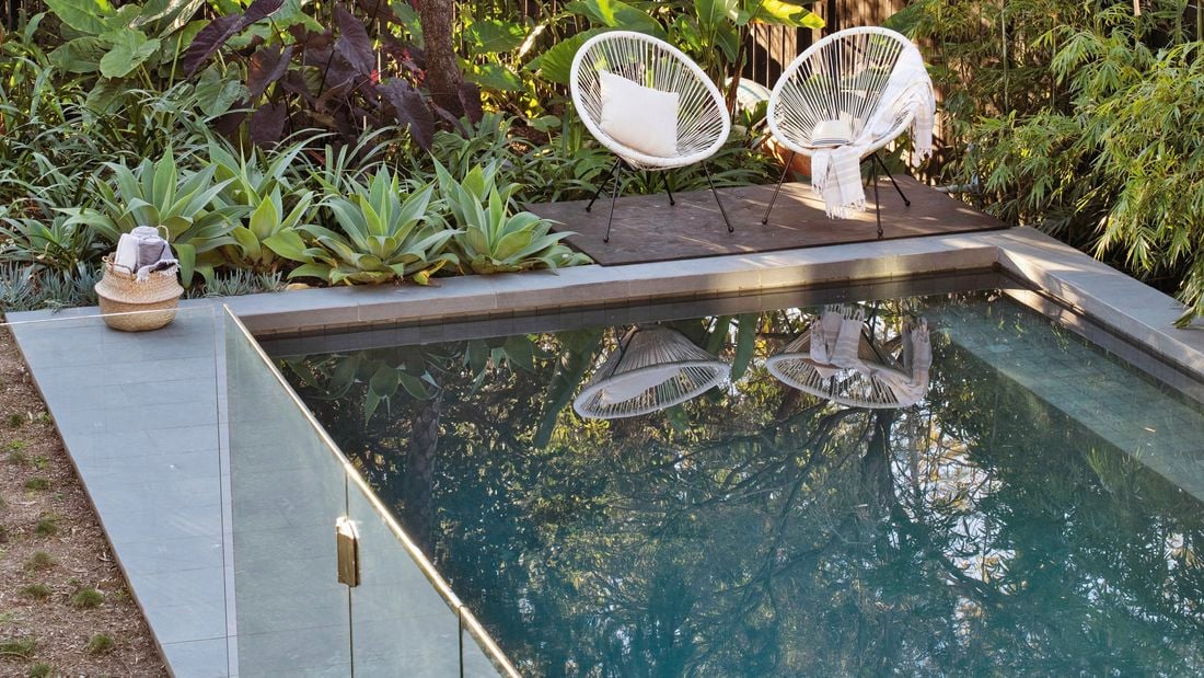 A pristine outdoor pool with deck chairs and lush green plants.
