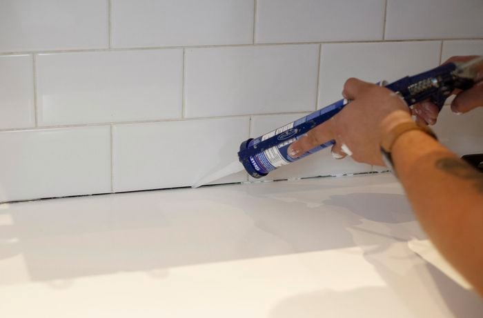 Person using caulking gun to add grout between kitchen bench and wall tiles.