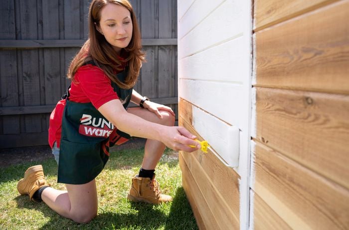 A Bunnings team member applying primer to the side of a wooden shed