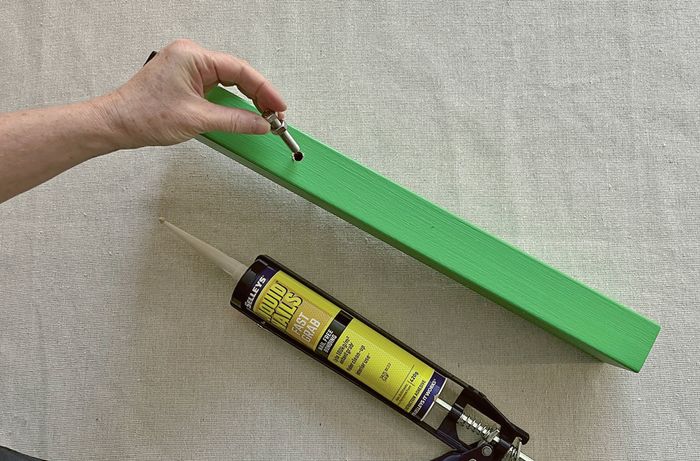 A hand inserting a hex head bolt into a drilled hole in a green block, with a cartridge of adhesive nearby.
