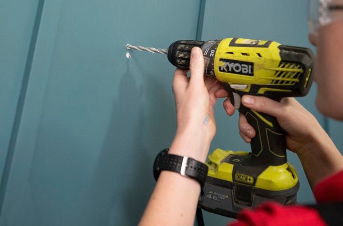 Person wearing safety glasses drilling into wall.