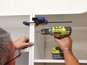Using a clamp and drill to secure the cabinets in the linen closet.