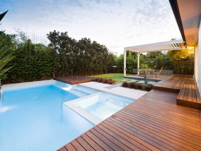 A pool with decking and trees around it.
