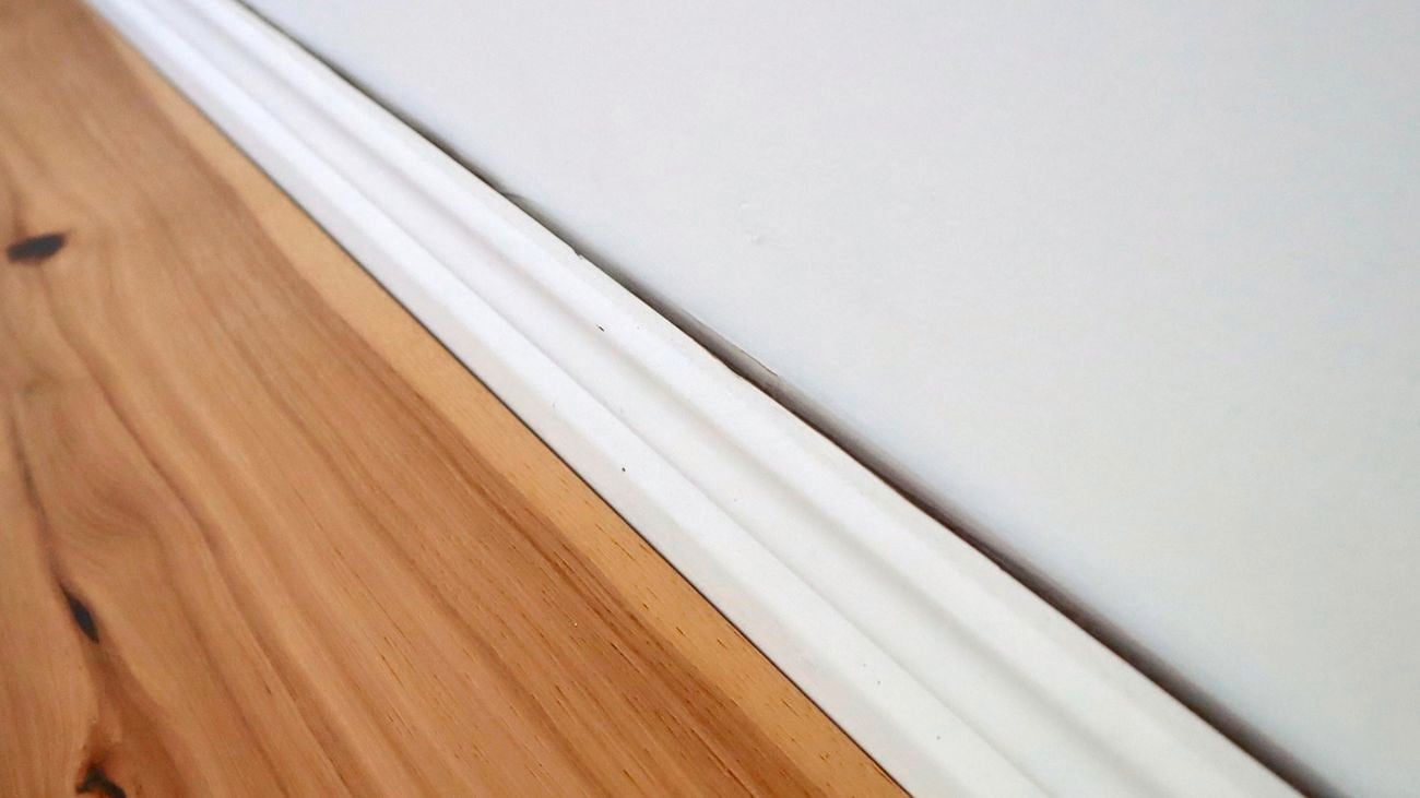 A gap between a skirting board and white wall.