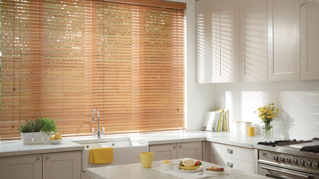 A white kitchen with wooden Venetian blinds.