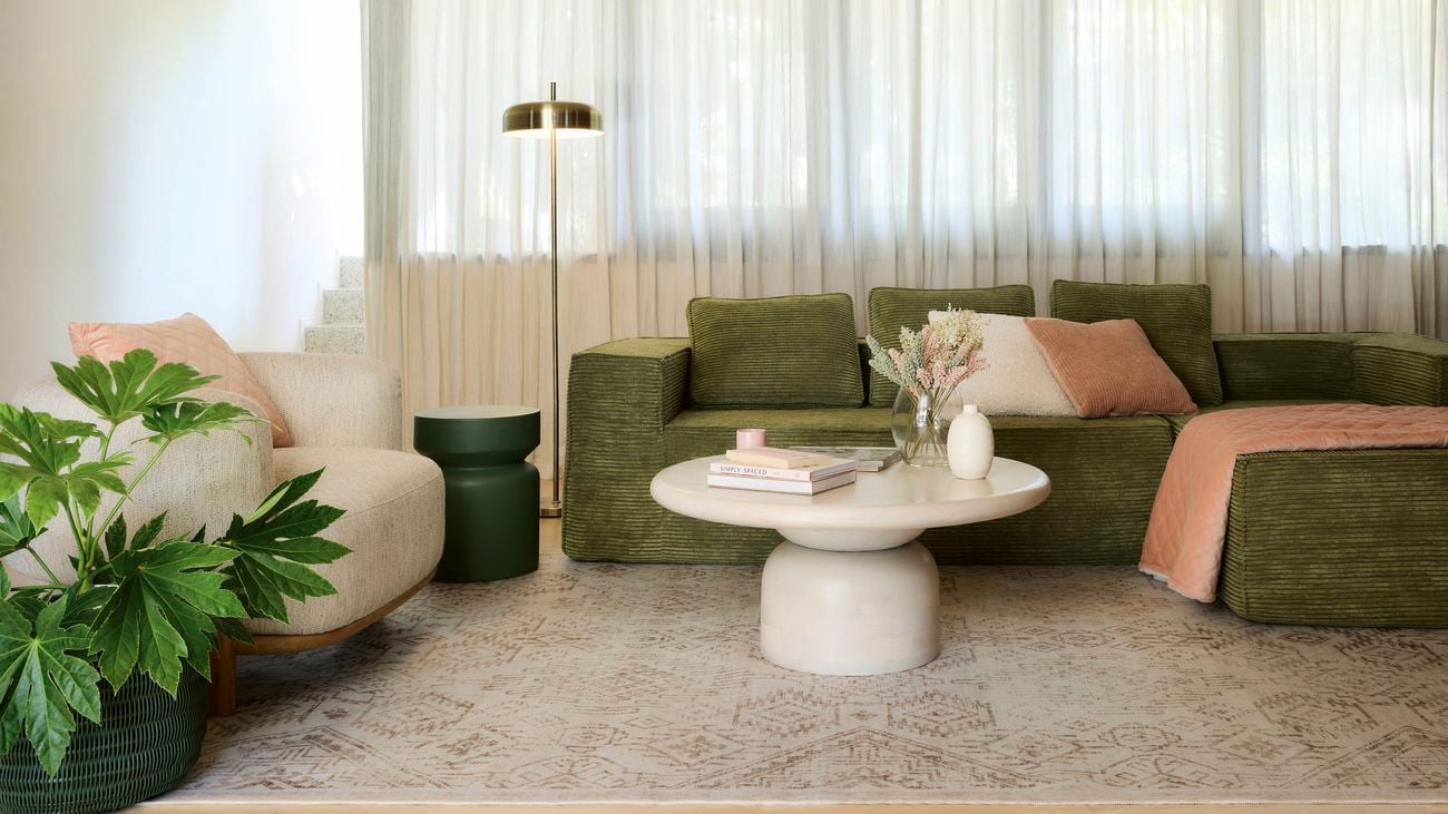 Living room while soft white sheer curtains, green and cream lounge with soft colour cream rug. 