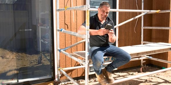 Person sitting on scaffolding outside and using a mobile phone