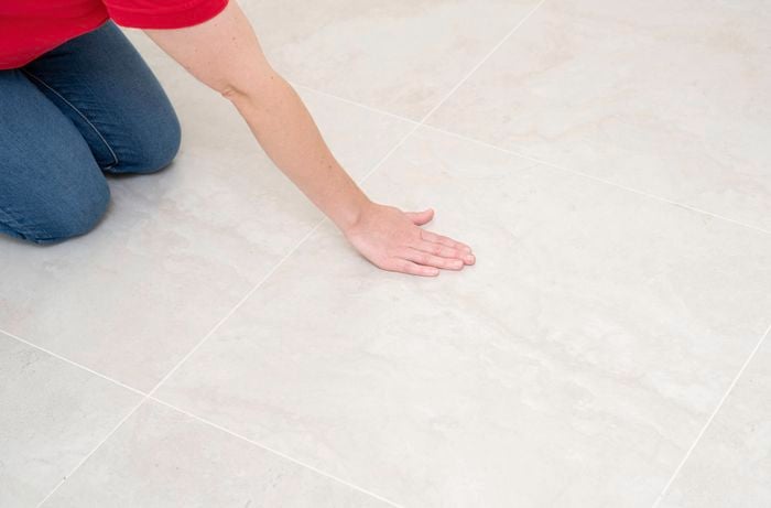 A person is inspecting ceramic tiles, a person highlights how simple finishes like laminate, melamine, and vinyl flooring offer durability and style at a lower price.