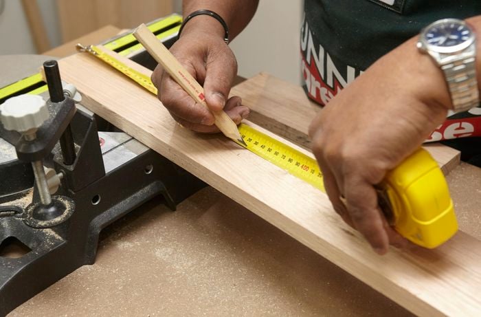 Person using measuring tape and pencil to mark up piece of ply wood.