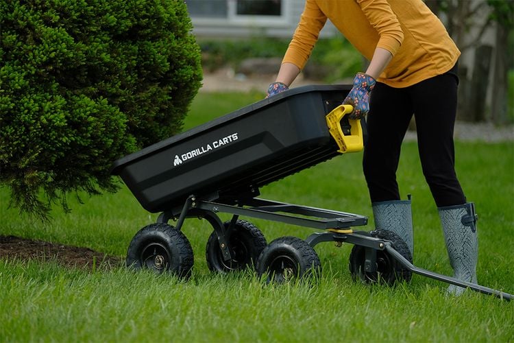 Woman tipping one end of a Gorilla cart up to empty fertiliser under a bush